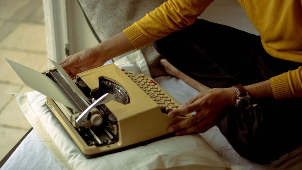 A person holding an off-white typewriter, inserting a sheet of paper.
